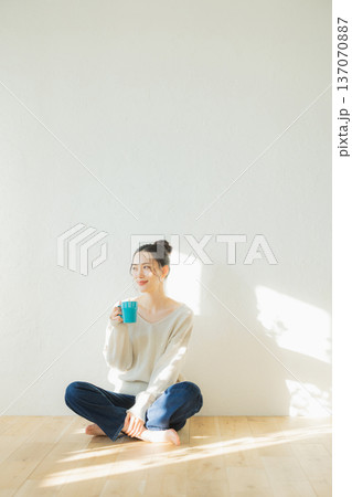 床に座ってコーヒーを飲む若い女性　 137070887