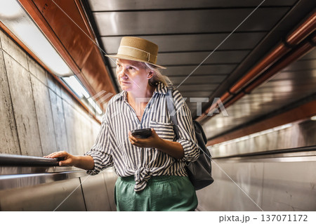 Middle-aged woman checking smartphone while riding escalator in subway passage Middle-aged woman checking smartphone while riding escalator in subway passage 137071172
