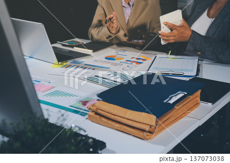 business documents on office table with tablet, smart phone and laptop and two colleagues discussing data business documents on office table with tablet, smart phone and laptop and two colleagues discussing data 137073038