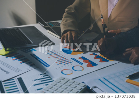 business documents on office table with tablet, smart phone and laptop and two colleagues discussing data 137073039
