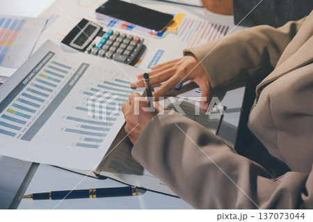 business documents on office table with tablet, smart phone and laptop and two colleagues discussing data business documents on office table with tablet, smart phone and laptop and two colleagues discussing data 137073044
