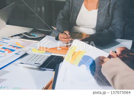 business documents on office table with tablet, smart phone and laptop and two colleagues discussing data 137073064