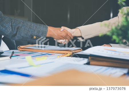 Entrepreneurs collaboration deal shaking hands in a modern office and financial paper graph on desk. 137073076