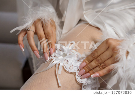 Elegant Bride Wearing White Lace Garter and Feathered Robe with Pink Nail Art in Soft Natural Light 137073830