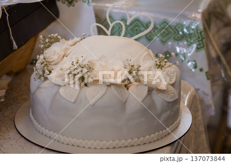 Elegant White Wedding Cake Decorated with Fresh Flowers and Heart Shaped Toppers on a Festive Table Setting Elegant White Wedding Cake Decorated with Fresh Flowers and Heart Shaped Toppers on a Festive Table Setting 137073844