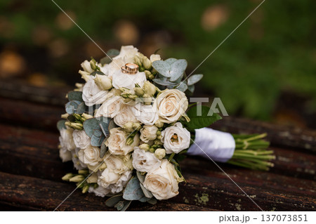 Elegant White Wedding Bouquet with Gold Rings on Rustic Wooden Surface, Soft Focus Background, Romantic and Natural Aesthetic 137073851
