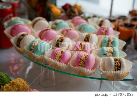 Colorful Macarons in Paper Cups Displayed on Glass Tray at Elegant Dessert Buffet with Pastel Hues and Textured Fillings 137073858