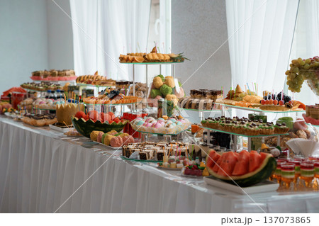 Elegant Buffet Table Overflowing with Assorted Desserts, Fruits, and Pastries in a Bright White-Room Setting 137073865