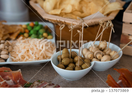 A vibrant charcuterie spread featuring olives, mushrooms, pistachios, and chips with rustic wooden textures and warm earthy tones 137073869
