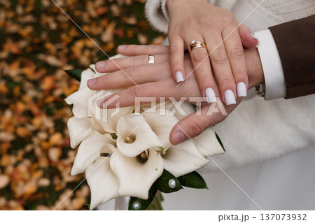 Close-up of Wedding Couple's Hands Holding White Calla Lilies Amid Autumn Leaves, Symbolizing Love and Marriage 137073932