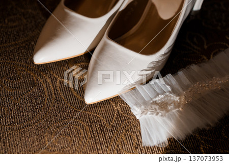 White Bridal Shoes with Tulle Garter on Textured Brown Carpet, Elegant Wedding Footwear Detail White Bridal Shoes with Tulle Garter on Textured Brown Carpet, Elegant Wedding Footwear Detail 137073953