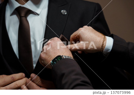 Close-Up of a Man Adjusting His Brown Tie and Pocket Square in a Black Suit with White Shirt 137073996