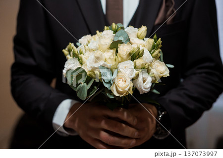 Elegant White Rose Bouquet Held by Groom in Black Suit at Wedding Ceremony 137073997