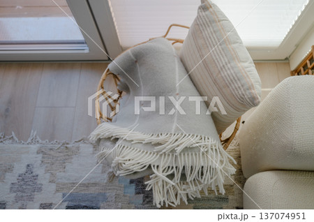 Rattan basket with soft blanket and pillow near window in cozy Scandinavian interior 137074951
