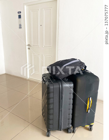 Two pieces of luggage stacked beside a closed white door in a rented apartment hallway, with a black backpack resting on top of a hard-shell suitcase 137075777