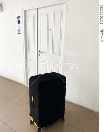 Black suitcase with yellow accents positioned in front of a closed white door in a hallway of a rented apartment, number 31 visible on the wall Black suitcase with yellow accents positioned in front of a closed white door in a hallway of a rented apartment, number 31 visible on the wall 137075780