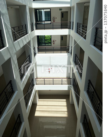 Modern multi-story building interior showcasing open atrium with natural light illuminating the space, featuring balconies and railings on each floor Modern multi-story building interior showcasing open atrium with natural light illuminating the space, featuring balconies and railings on each floor 137075840