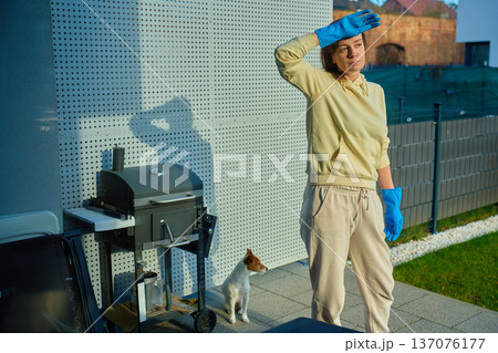 Woman standing on home terrace wearing protective gloves near barbecue grill Woman standing on home terrace wearing protective gloves near barbecue grill 137076177