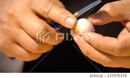 A chef is peeling shallots with a small sharp kitchen knife for preparing the ingredient process. Holding a shallot in hands. A chef is peeling shallots with a small sharp kitchen knife for preparing the ingredient process. Holding a shallot in hands. 137076376