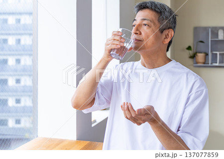 窓辺で薬を飲むシニア男性 窓辺で薬を飲むシニア男性 137077859