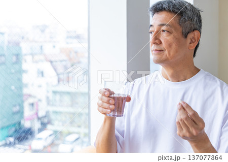 窓辺で薬を飲むシニア男性 137077864