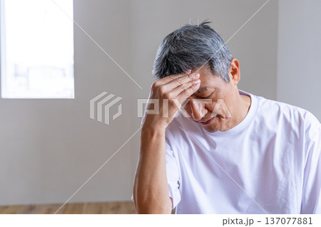 リビングで頭を抱えるシニア男性 137077881