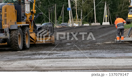 Construction machinery operates on a road at a work site in an urban area during daylight hours 137079147