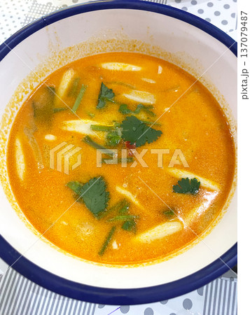Thai Tom Yum soup in a white bowl with a blue rim, featuring herbs and spices, viewed from above on a patterned tablecloth Thai Tom Yum soup in a white bowl with a blue rim, featuring herbs and spices, viewed from above on a patterned tablecloth 137079487