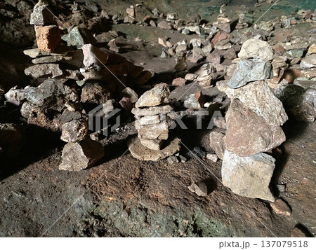 Stone cairns arranged in a cave setting, showcasing various sizes and shapes of rocks on the ground, with a natural earthy background and dim lighting 137079518