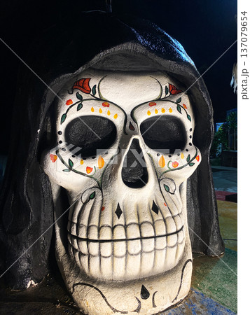 Large decorative skull with intricate floral patterns and vibrant colors, illuminated at night, showcasing Halloween-themed decor in a city center setting Large decorative skull with intricate floral patterns and vibrant colors, illuminated at night, showcasing Halloween-themed decor in a city center setting 137079654