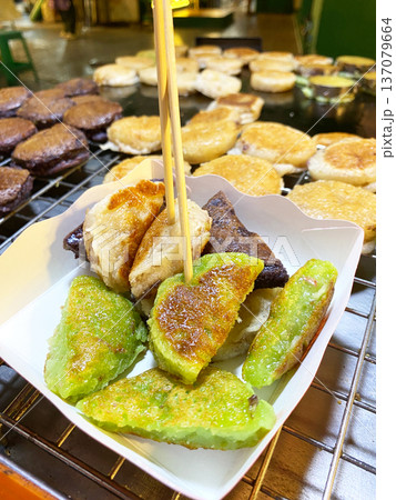 Coconut pancakes served in a white paper container with wooden skewers, featuring green and brown varieties, displayed at a street food stall in Asia 137079664