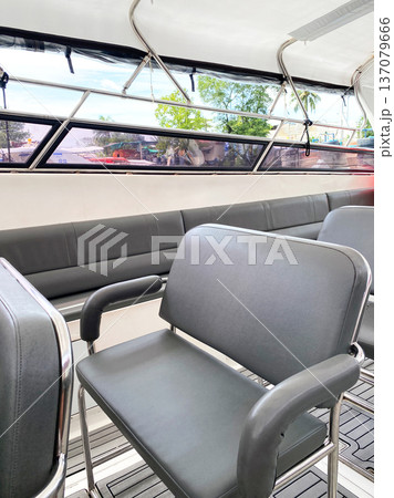 Empty seats on a tourist boat with gray cushioned chairs and large windows providing views of the surrounding landscape and natural light 137079666