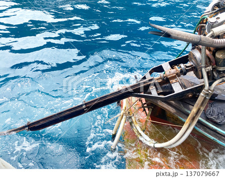 Outboard motor mounted on a fishing boat with a propeller submerged in clear blue ocean water, showcasing mechanical components and water splashes 137079667