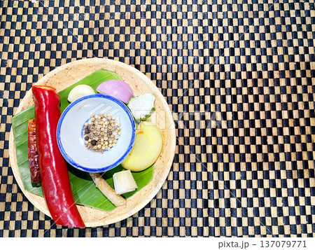 Assorted spices and fresh ingredients for preparing Thai cuisine arranged on a woven bamboo mat, showcasing vibrant colors and textures in a circular bamboo plate 137079771
