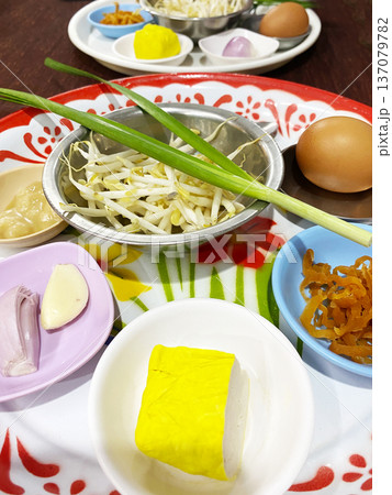 Ingredients for making classic Pad Thai displayed on colorful plates, including cabbage, eggs, garlic, and yellow tofu, arranged on a wooden table 137079782