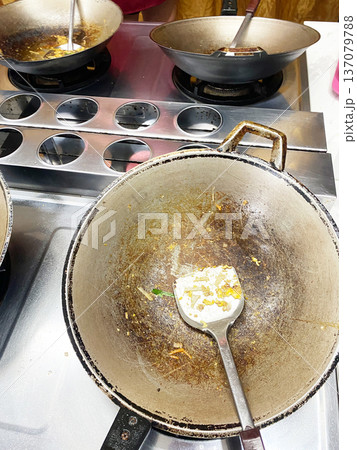 Wok and frying pans on a stainless steel stove with remnants of food, cooking utensils, and a clean surface indicating a culinary master class setting Wok and frying pans on a stainless steel stove with remnants of food, cooking utensils, and a clean surface indicating a culinary master class setting 137079788