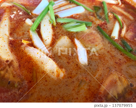 Close-up view of tom yum soup featuring sliced mushrooms, green onions, and a rich, spicy broth in a bowl, highlighting vibrant colors and textures 137079955