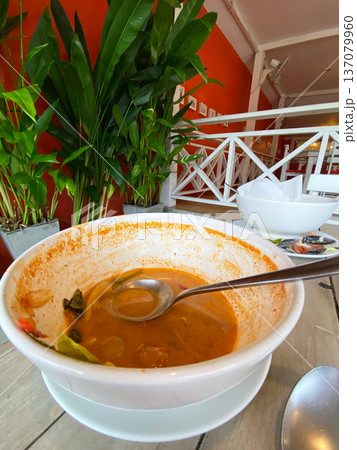 Empty bowl with remnants of soup and a spoon resting inside, surrounded by green plants and a bright orange wall in a modern dining setting 137079960