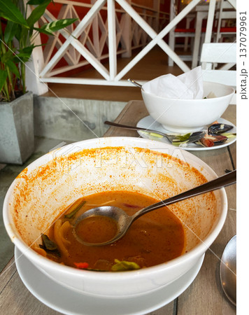Empty bowl with remnants of soup and vegetables on a wooden table, a second bowl and napkin holder visible in a casual dining setting Empty bowl with remnants of soup and vegetables on a wooden table, a second bowl and napkin holder visible in a casual dining setting 137079961