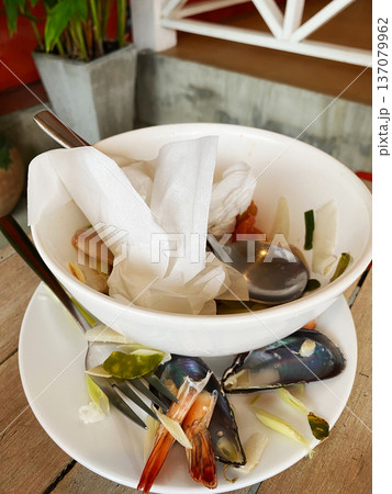 Empty white bowl with remnants of seafood and vegetables on a plate, accompanied by utensils, set on a wooden table in a casual dining environment Empty white bowl with remnants of seafood and vegetables on a plate, accompanied by utensils, set on a wooden table in a casual dining environment 137079962