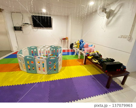 Children's play area in a cafe featuring colorful mats, a plastic playpen, toys, and a television on the wall, designed for young children to enjoy Children's play area in a cafe featuring colorful mats, a plastic playpen, toys, and a television on the wall, designed for young children to enjoy 137079963