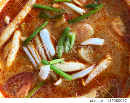 Close-up top view of vibrant tom yum soup featuring sliced mushrooms, green onions, and spices in a rich broth, served in a bowl with a colorful presentation 137080087