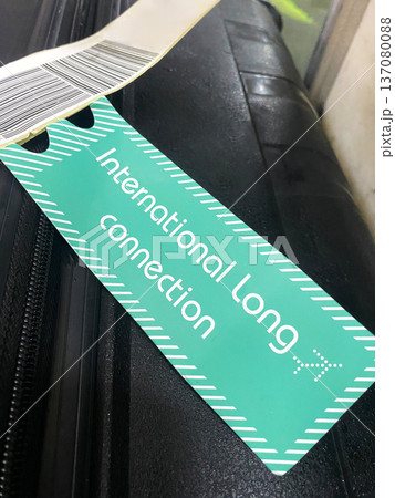 Luggage tag displaying "International Long Connection" text attached to a black suitcase with a barcode visible on a travel surface Luggage tag displaying "International Long Connection" text attached to a black suitcase with a barcode visible on a travel surface 137080088
