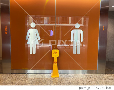 Airport restroom entrance featuring gender symbols for women and men, with a caution sign indicating maintenance in a modern terminal setting Airport restroom entrance featuring gender symbols for women and men, with a caution sign indicating maintenance in a modern terminal setting 137080106