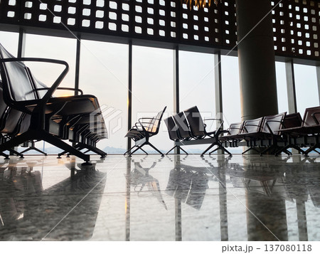 Airport waiting room featuring modern seating arrangements with large windows showcasing a scenic view of the outdoors and a polished marble floor reflecting the interior design Airport waiting room featuring modern seating arrangements with large windows showcasing a scenic view of the outdoors and a polished marble floor reflecting the interior design 137080118