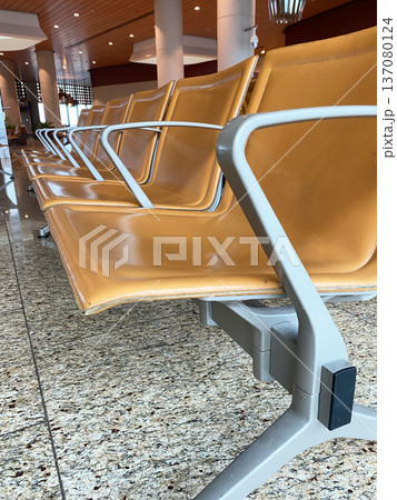 Airport waiting area featuring modern orange seating with metal frames, polished granite flooring, and bright overhead lighting in a spacious terminal environment 137080124