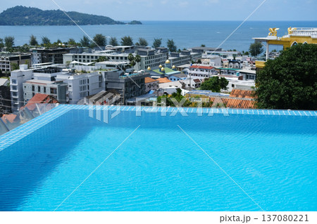 Infinity pool overlooking coastal cityscape with ocean view, lush hills in the background, and modern buildings lining the waterfront under a clear blue sky 137080221