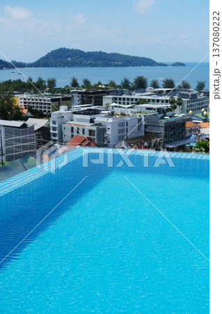 Rooftop swimming pool with clear blue water overlooking a coastal cityscape and distant island under a bright blue sky with scattered clouds 137080222