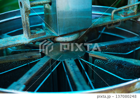 Honey extractor machine with metal components and mesh screens, used for separating honey from honeycombs in a beekeeping operation 137080248