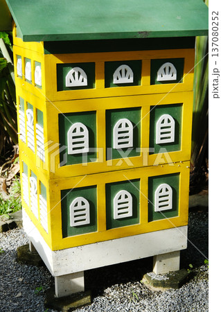 Beehive model designed as a fairytale house with colorful yellow and green exterior, featuring decorative windows and a sloped roof in a garden setting 137080252